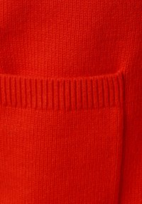 Czerwona dzianinowa tekstura swetra z ribbowanym dołem i małym detalem kieszonki. Gładka powierzchnia o jednolitym kolorze i regularnym wzorze splatania.