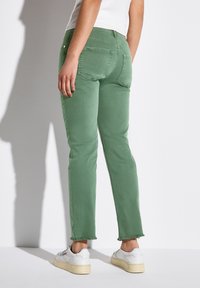 Gröna denimjeans med en kortad passform, fransade fållar och två bakfickor. Matchas med vita sneakers och en tät vit topp.