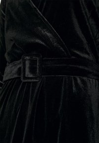 Svart sammetklänning med en inslagning design, texturerad tyg och ett brett bälte med en fyrkantig spänne, som framhäver eleganta linjer och en slät finish.