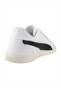 Zapatilla de piel blanca con diseño de acento negro, que presenta una franja lateral texturizada y una suela de goma color crema. Logo dorado en el talón.