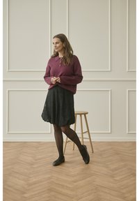 Violetinės megztos palaidinės su apykakle, derinamos su juoda raštuota sijonu. Juodos pėdkelnės ir plokšti bateliai užbaigia įvaizdį.