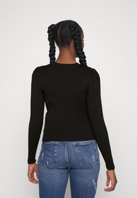 Haut noir côtelé à manches longues avec épaules bouffantes, associé à un jean bleu déchiré. Le haut présente une coupe ajustée et un col rond.