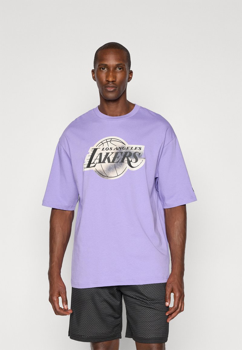 Tricou oversized lila din bumbac, cu un grafic argintiu ce prezintă o minge de baschet și textul "Los Angeles Lakers". Asortat cu pantaloni scurți din plasă negri.