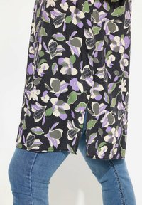 Tunica floreale con sfondo nero, caratterizzata da fiori viola e verdi. Tessuto leggero, con spacco laterale, abbinata a jeans blu.