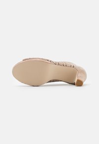 Zapato de ante beige de tacón bajo tumbado de lado, mostrando la suela lisa con un ligero estriado cerca del dedo del pie y un pequeño tacón cuadrado.