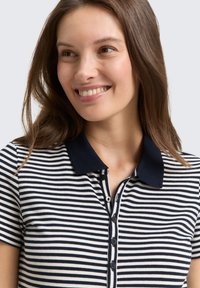 Marineblå og crème-stribet polo med krave, korte ærmer, en knaplukning og en blød tekstur. Den tætsiddende pasform fremhæver silhuetten.