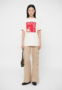 Κρέμα μπλουζάκι με κόκκινο τετράγωνο γραφικό και λογότυπο, συνδυασμένο με μπεζ cargo παντελόνι που έχει πλαϊνές τσέπες και χαλαρή εφαρμογή.