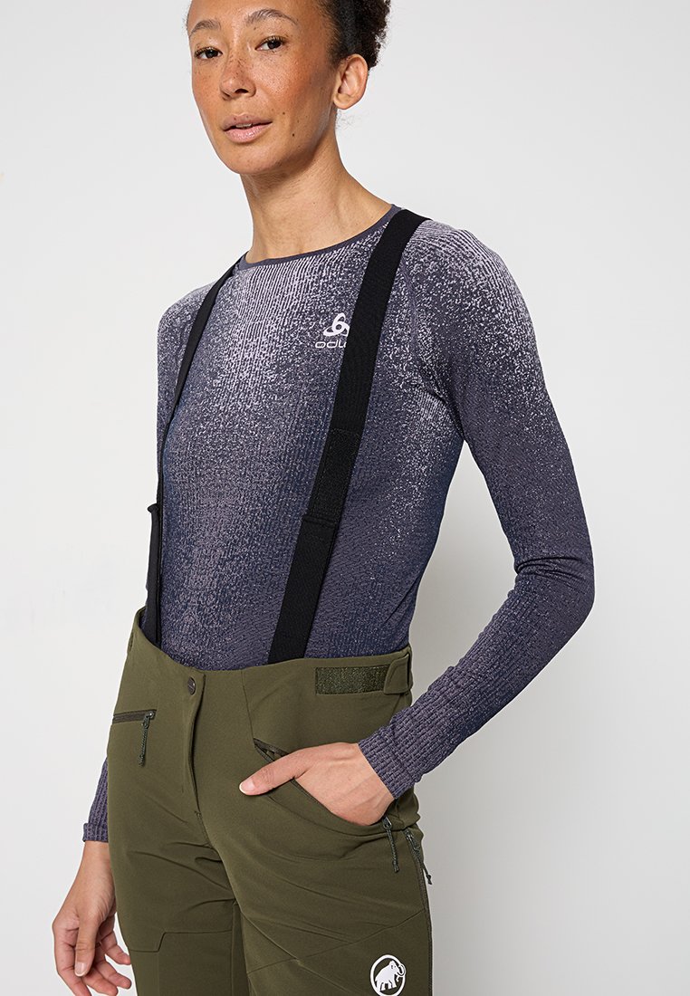 Langärmliges lila Top mit strukturiertem Muster und Logo, kombiniert mit olivgrünen Hosen mit verstellbaren Trägern und Reißverschlusstaschen.