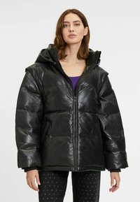 Zwarte pufferjack met een glanzende leren afwerking, grote capuchon, rits aan de voorkant en een oversized silhouet. Beschikt over gestikte secties en ribgebreide cuffs.