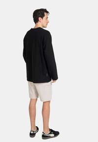 Camisa negra de manga larga con un corte relajado, combinada con pantalones cortos de carga beiges. La persona lleva zapatillas negras. Diseño simple y minimalista.