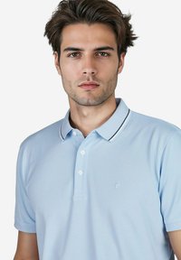 Lichtblauwe polo gemaakt van textuurstof, met een kraag met zwarte accenten, een knoopsluiting met drie knopen en een klein logo op de borst.