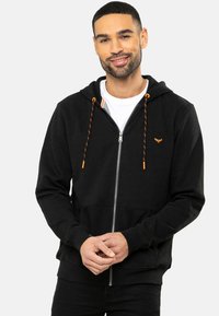 Sort zip-up hoodie lavet af bomuldsblanding, med orange snore, forlommer og et lille logo på venstre bryst.