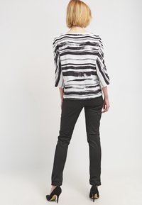 Blouse rayée noir et blanc à manches trois-quarts, associée à un pantalon noir ajusté et des escarpins noirs.