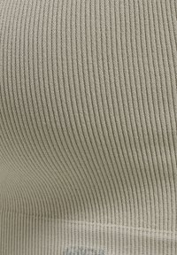 Ribbade linne i ljusbeige tyg, med en sömlös design och mjuk textur. Inkluderar en liten logotypdetalj nära botten.