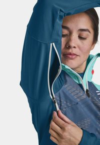 Hiking jacket in teal and light blue, featuring a zippered front, mesh detailing, and contrasting accents. Material appears smooth and durable.