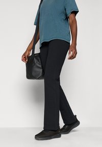 Fekete, testhez simuló leggings, laza, türkiz színű felsővel párosítva, fekete hálós tornacipővel. Egy kis fekete táska van az egyik kezében.