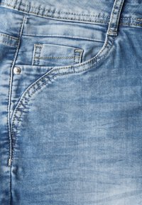 Jeans de mezclilla azul claro con una cintura de media altura, costuras detalladas y un pequeño bolsillo delantero. La textura desgastada añade un carácter sutil.
