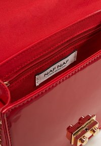 Czerwona torebka ze skóry lakierowanej o gładkiej fakturze, z wewnętrzną kieszenią na zamek i zapięciem w kolorze złotym z przodu.