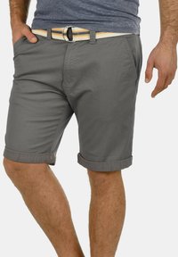 Grijze katoenen shorts met opgerolde manchetten, zijzakken en een gevlochten riem met een patroon van gele en marineblauwe strepen. Gladde textuur en casual ontwerp.