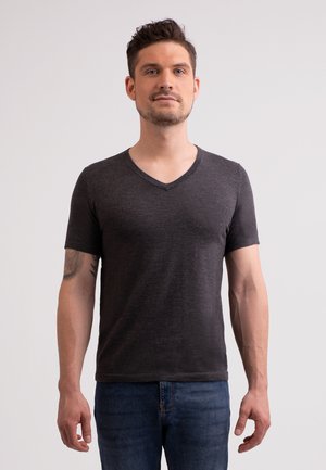 Camiseta negra de cuello en V hecha de tela suave, con mangas cortas y un corte relajado, combinada con jeans azules. Diseño simple sin patrones.