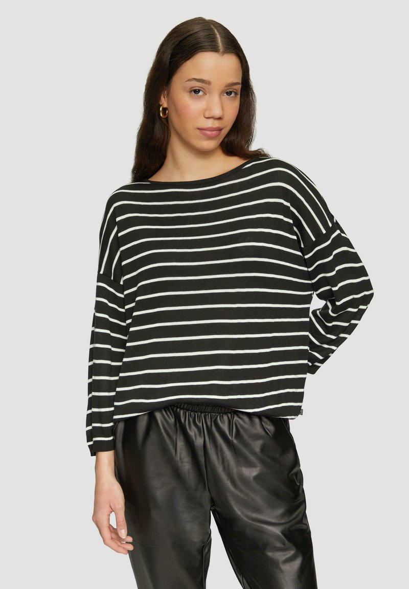 Zwart-wit gestreepte sweater met een brede halslijn en een losse pasvorm, gecombineerd met zwarte leren joggerbroeken. Zachte textuur en relaxte silhouet.
