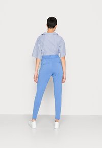 Blauwe elastische broek met een blauwe en witte gestreepte kortekouterhemd. Model draagt witte sneakers. Glad textuur van de stof.