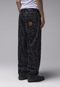 Μαύροι φαρδιοί παντελόνες με διακοσμητικό μοτίβο και υφασμάτινη υφή. Διαθέτουν πίσω τσέπη και δερμάτινο διακοσμητικό σημείο. Συνδυάζονται με μαύρες μπότες.