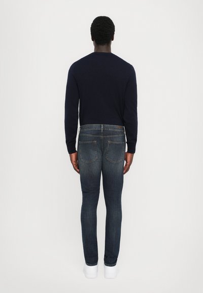 Maglione navy e jeans slim-fit blu scuro. Materiale morbido, design semplice, stile a cinque tasche, con sneakers bianche. Estetica pulita e minimale.