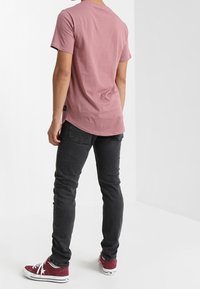 Camiseta de manga corta y cuello redondo en color rosa apagado, combinada con jeans oscuros ajustados y zapatillas burdeos, mostrando una vista trasera sencilla.