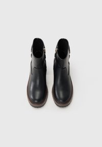 Pair of black leather ankle boots with brown soles and side zippers, viewed from above on a light background.