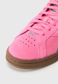 Roze suede tenisice s teksturiranom površinom, perforacijama za prozračnost i kontrastnim zelenim logom, upotpunjene smešnim gumenim potplatom.
