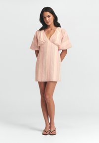 Vestito corto rosa con scollo a V, maniche corte e larghe, e righe verticali in tonalità chiare. Realizzato in un tessuto morbido e testurizzato.