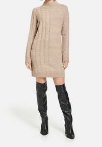 Robe pull en tricot beige avec poignets côtelés et col montant, présentant un motif zigzag texturé et une coupe ample jusqu'au milieu des cuisses.