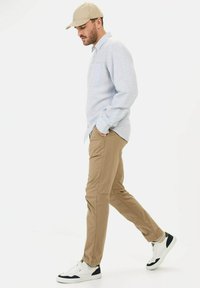 Himmelblaues Langarmhemd mit Tasche, khakifarbene Hose und weiße Sneakers mit marineblauen Akzenten; männliches Model, das vor einem schlichten Hintergrund geht.