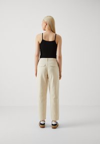Beige högmidjade byxor med rak passform, med två bakfickor, tillsammans med en åtsittande svart tanktop och avslappnade skor.