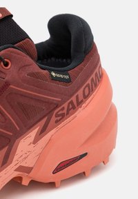 Gros plan sur une chaussure de trail Salomon bordeaux et corail avec tissu Gore-Tex et semelle Contagrip pour une adhérence optimale.
