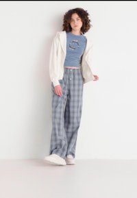 Lichte beige zip-up hoodie, blauwe grafische crop top en grijs geruite wijde broek. Witte sneakers maken de outfit complete.