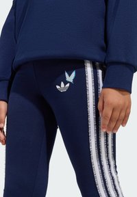 Mornarsko plave tajice s bijelim volanima sa strane, s bijelim Adidas logom i plavim leptirom na bedro. Mekani materijal.