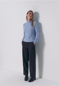 Pull côtelé bleu clair à col montant, associé à un pantalon ample foncé et des bottines noires. Design simple et moderne.
