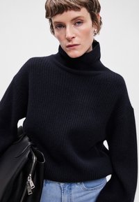 Σκούρο ναυτικό μπουφάν με ριβέ υφή και χαλαρή εφαρμογή. Συνδυασμένο με μια κομψή μαύρη τσάντα, που διαθέτει ασημένια λεπτομέρεια φερμουάρ και υφασμάτινες λεπτομέρειες.