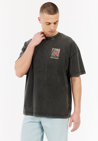 Grijze oversized t-shirt met korte mouwen, voorzien van een kleurrijk bedrukt logo-ontwerp op de borst en een licht versleten textuur.