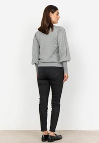 Harmaa neule, jossa on pullistuvat hihat ja ribbaushelma, yhdistettynä mustiin slim-fit farkkuihin ja mustiin kenkiin. Yksinkertainen muotoilu, pehmeä rakenne.