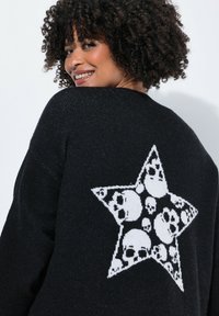 Pull noir avec un grand motif d'étoile blanche et des motifs de crâne. Tissu doux et texturé avec une coupe ample.