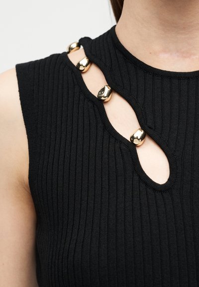 Gros plan sur un haut sans manches noir côtelé avec un col torsadé orné de quatre perles dorées brillantes.