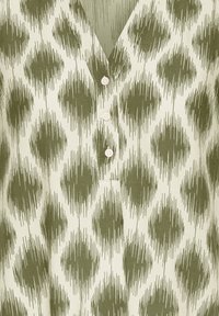 Lyst stof med et grønt abstrakt prikket mønster og tre små hvide knapper på et V-hals-tøj.