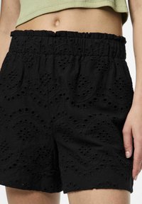 Svarta shorts av texturerad kvalitet, med ett broderat mönster med utskärningar och en elastisk, volangmidja.