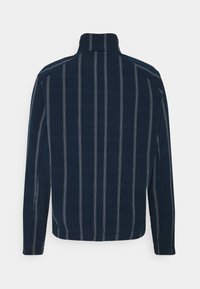 Mörkblå långärmad skjorta med vertikala vita ränder, en stående krage och rak nederkant. Tyget verkar slätt och lätt.