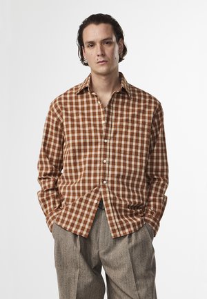 Brown and white checkered shirt with a collar, front buttons, and long sleeves, paired with high-waisted gray trousers.