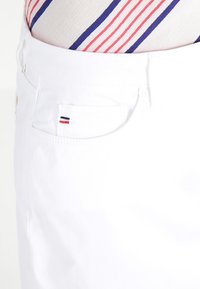 Witte denim shorts met een voorzak met een klein rood, wit en blauw logo. De stof lijkt soepel en lichtgewicht.