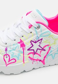 Białe sneakersy z kolorowymi wzorami graffiti w kształcie gwiazdek i serc w odcieniach różu, niebieskiego i zielonego. Posiadają białe sznurówki i wnętrze z różowymi akcentami.